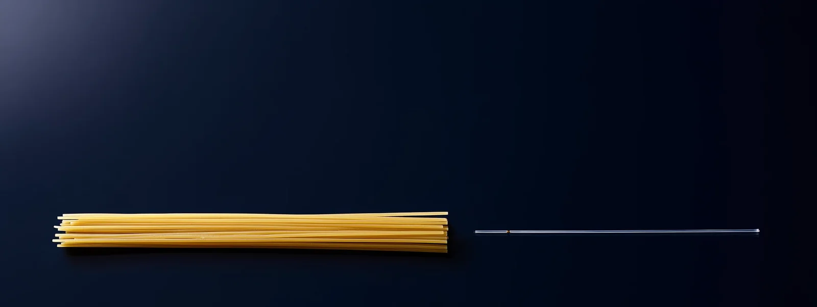 La fibra de 600 µm junto a un fideo de espagueti: la escala explica por qué el acceso es una punción, y no una incisión.